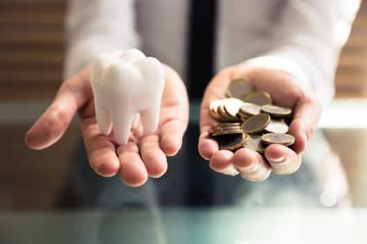 person holding an oversized tooth object in one hand and coins in the other hand