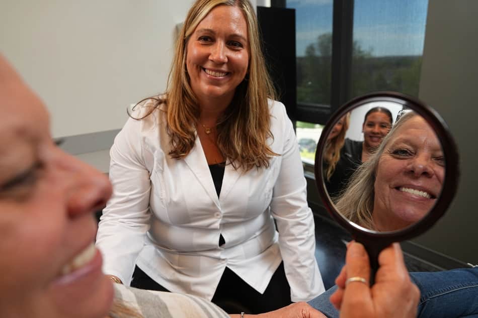 Amy smiling while looking in a mirror with Dr. Hedrick after her All-on-X dental implant treatment at Longmont Dental Loft